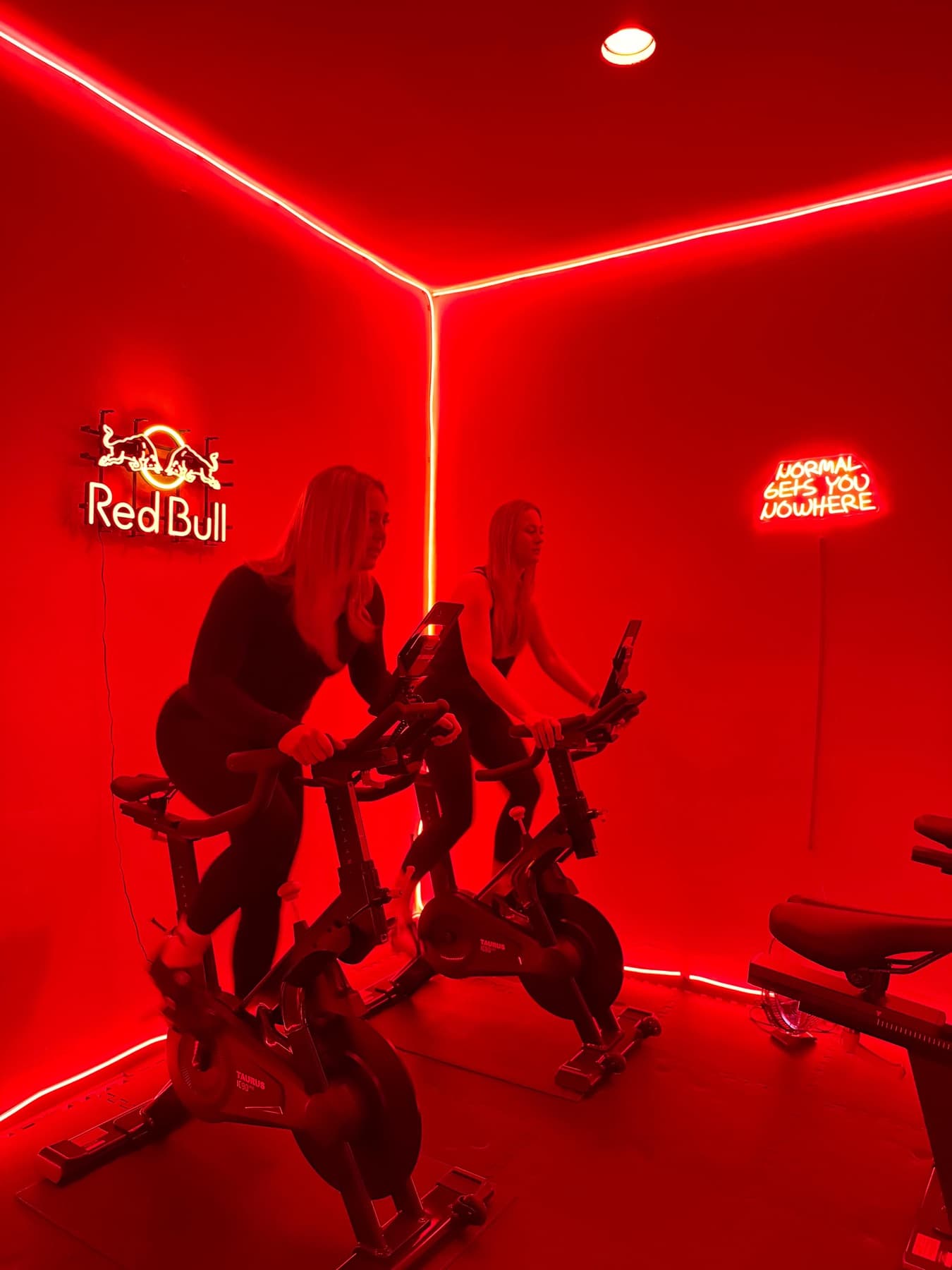 Zwei Frauen auf Bikes im roten Skylon-Cube, Neonlicht an Decke und Wänden